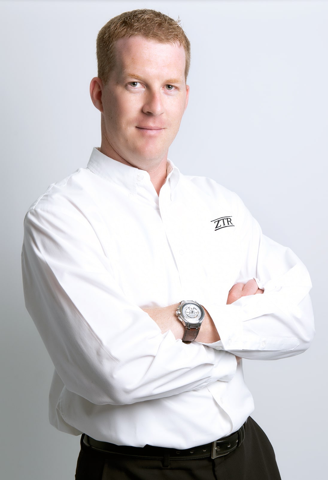 Man in white shirt with watch, arms crossed.