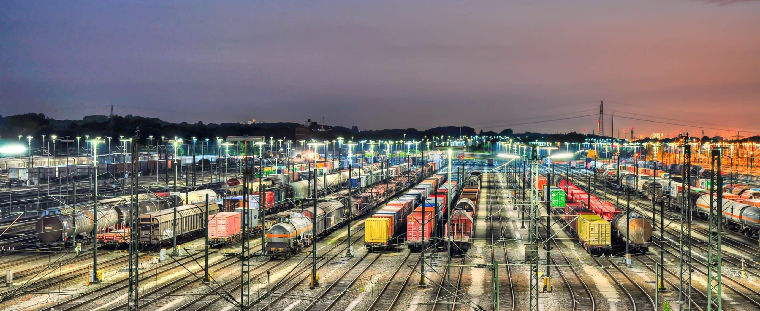 Colorful cargo trains at night in a rail yard.