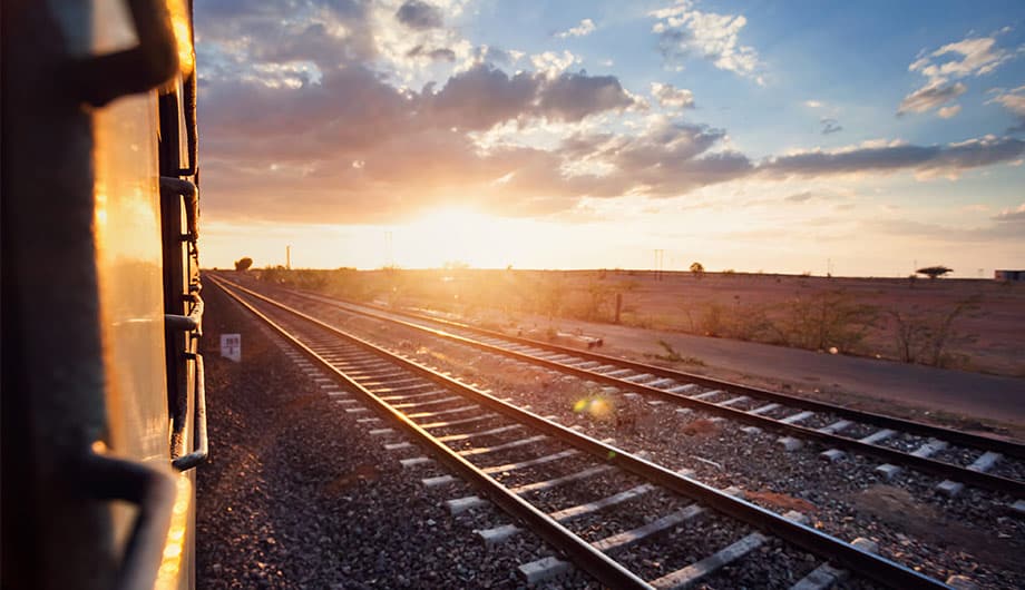 Sunset view from moving train, tracks visible.