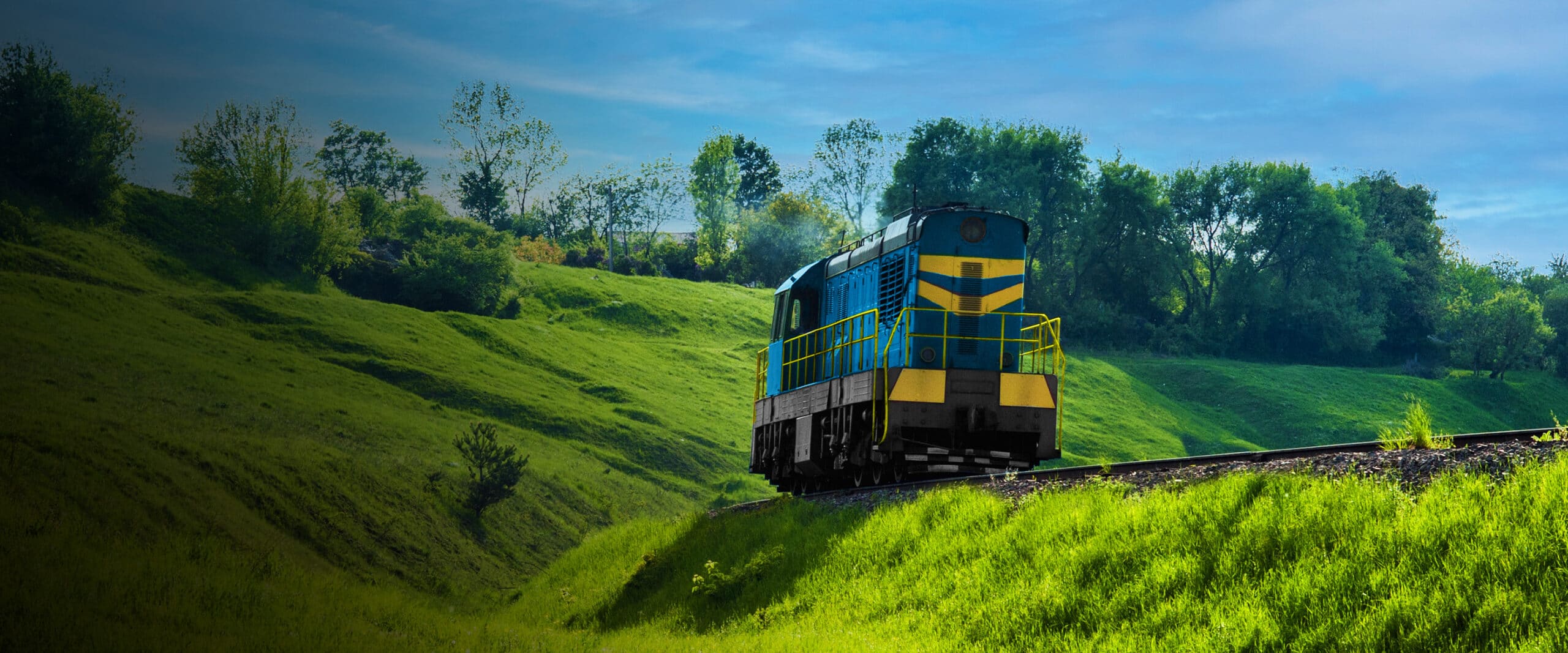 Blue train travels through scenic green landscape